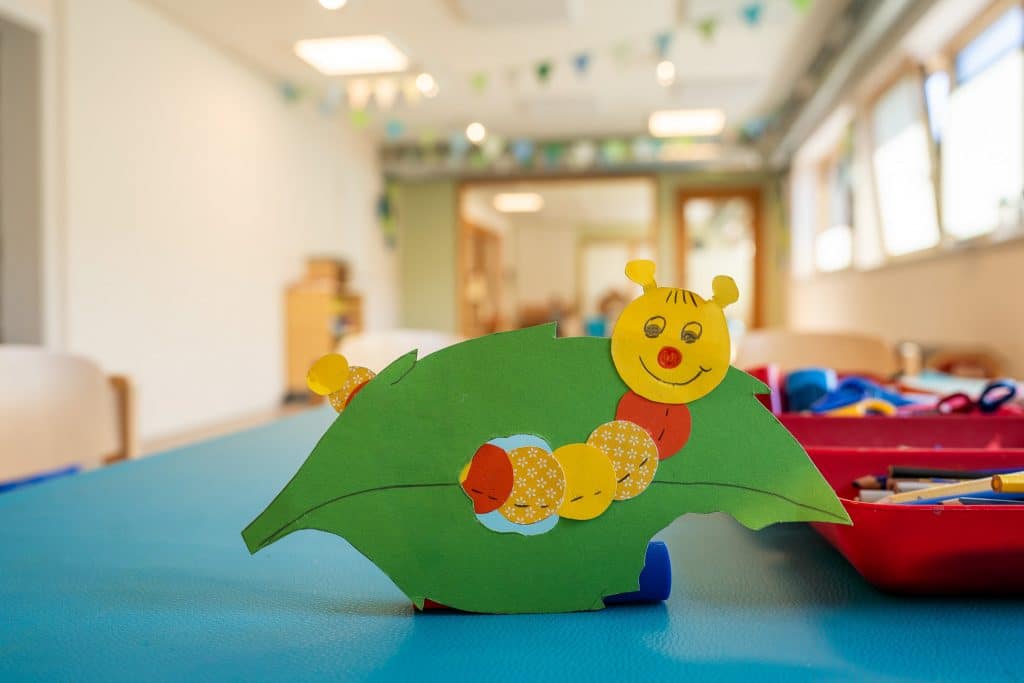 Bunte Raupe auf grünem Blatt aus Tonkarton auf einem Basteltisch mit Bastelutensilien
