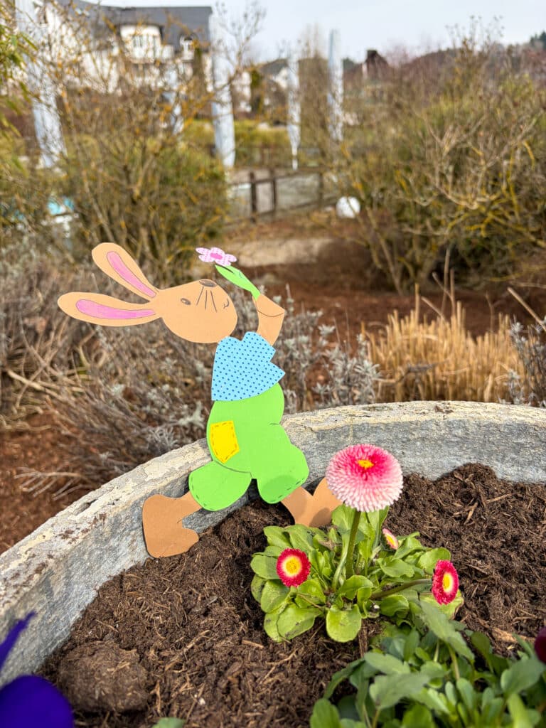 Osterhase aus Tonkarton gebastelt in einem Blumenkasten mit roten Blüten