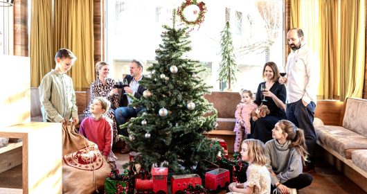 Familie versammelt um den Weihnachtsbaum mit großer roter Spielzeugeisenbahn und Geschenken