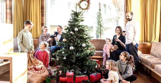 Familie versammelt um den Weihnachtsbaum mit großer roter Spielzeugeisenbahn und Geschenken