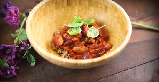 Bohneneintopf in einer hellen Holzschale mit Basilikum garniert