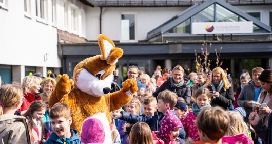 Eine Gruppe von Erwachsenen und Kindern umringen den Osterhasen auf der Spielstraße vom Familotel Sonnenpark