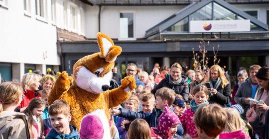 Eine Gruppe von Erwachsenen und Kindern umringen den Osterhasen auf der Spielstraße vom Familotel Sonnenpark