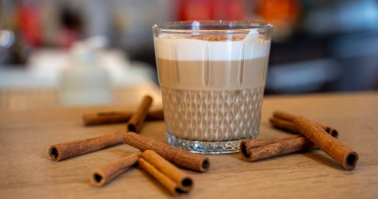Chai Latte mit Zimstangen und Kardamom im Glas auf einer Holztheke