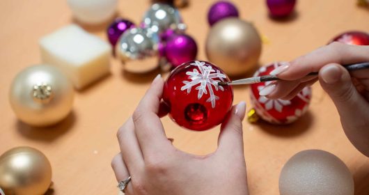 handbemalte Weihnachtskugel in rot mit einer weißen Schneeflocke als Motiv umringt von weiteren Weihnachtskugeln