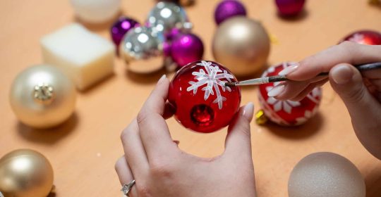 handbemalte Weihnachtskugel in rot mit einer weißen Schneeflocke als Motiv umringt von weiteren Weihnachtskugeln