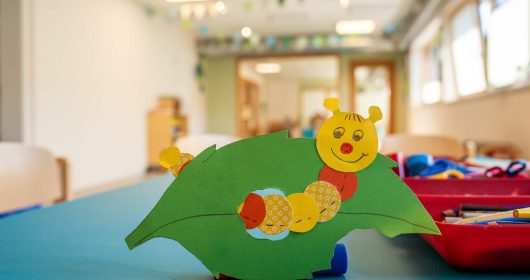 Bunte Raupe auf grünem Blatt aus Tonkarton auf einem Basteltisch mit Bastelutensilien