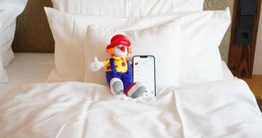 Happy Clown Familotel Maskottchen auf einem Bett mit Gute Nacht Geschichten vom Sonnenpark