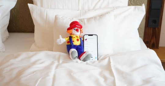 Happy Clown Familotel Maskottchen auf einem Bett mit Gute Nacht Geschichten vom Sonnenpark