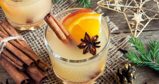 Glas gefüllt mit Apfelpunsch, Orange, Zimtstange und Sternanis umgeben von Weihnachtsdekoration
