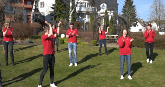 Kinderbetreuer in roten Outfits tanzen auf grünem Rasen im Sonnenschein