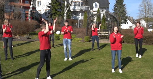 Kinderbetreuer in roten Outfits tanzen auf grünem Rasen im Sonnenschein