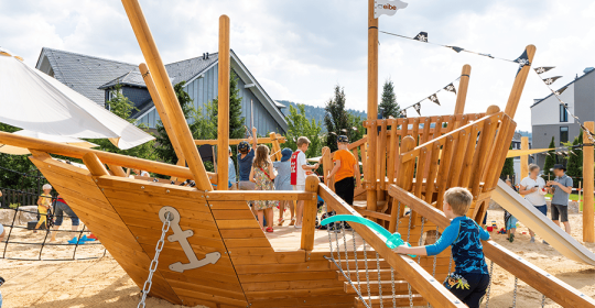 hölzernes Piratenschiff auf Spielplatz mit spielenden Kindern