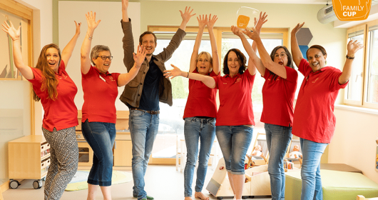 Kinderbetreuer werfen die Arme in die Luft und halten den Family-Cup Award in den Händen