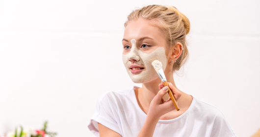 Frau trägt sich eine Beauty Maske für sonnengeschädigte Haut mit Pinsel im Gesicht auf