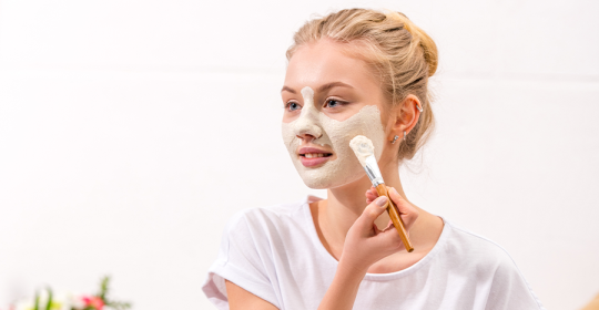 Frau trägt sich eine Beauty Maske für sonnengeschädigte Haut mit Pinsel im Gesicht auf