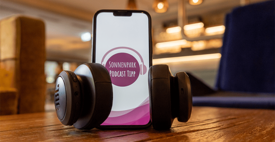 Smarthpone auf einem Holztisch in einer Lounge, umgebundene Kopfhörer