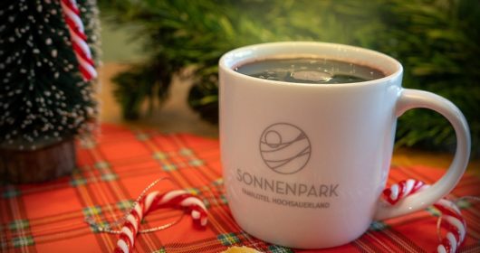 Glühwein in weißer Tasse umgeben von weihnachtlicher Dekoration