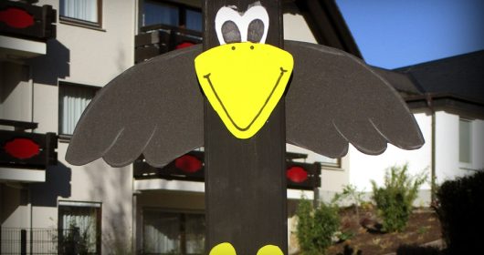 Zaunlattenfigur in Form eines Rabens vor einem HAus mit Balkonen