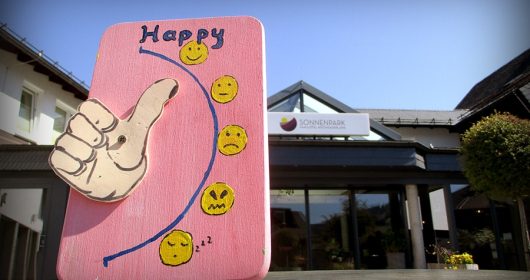 rosa Brett mit Daumen und Smileys vor Hoteleingang