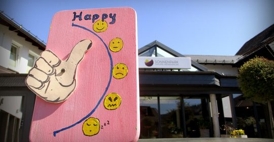 rosa Brett mit Daumen und Smileys vor Hoteleingang