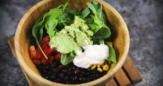 Mexikanische Burrito Bowl mit Bohnen, Mais, Salat und Guacamole in einer Holzschüssel