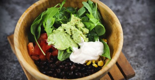 Mexikanische Burrito Bowl mit Bohnen, Mais, Salat und Guacamole in einer Holzschüssel
