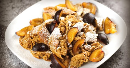 veganer Kaiserschmarrn mit Pflaumen und Puderzucker auf einem weißen Teller