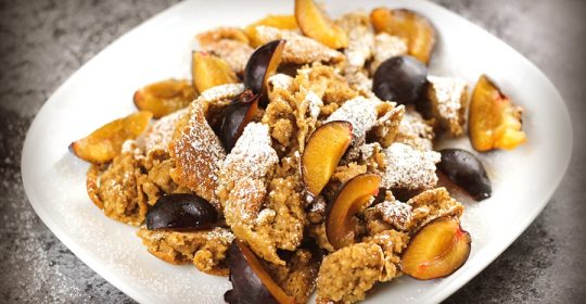 veganer Kaiserschmarrn mit Pflaumen und Puderzucker auf einem weißen Teller
