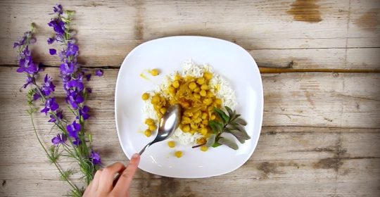 Kichererbsen Curry auf weißem Teller mit Blumendekoration auf einem Holztisch