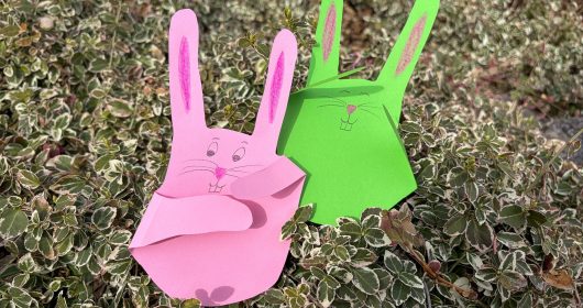 ein pinker und ein grüner gebastelter Hase aus Tonpapier in einem Busch