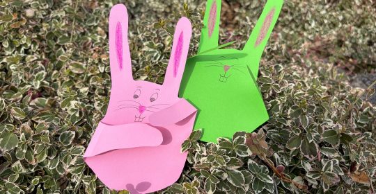 ein pinker und ein grüner gebastelter Hase aus Tonpapier in einem Busch
