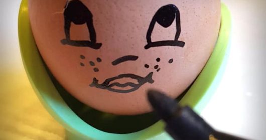 Ausgehöhltes Ei in grünem Eierbecher wird mit schwarzem Edding bemalt