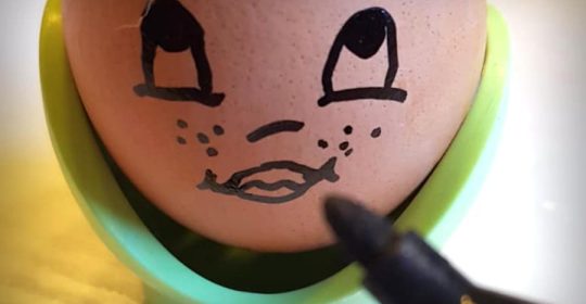 Ausgehöhltes Ei in grünem Eierbecher wird mit schwarzem Edding bemalt