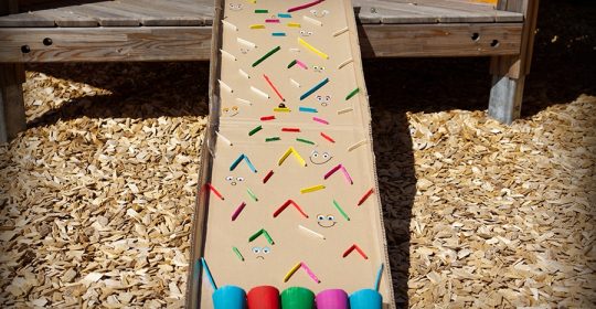 Murmelbahn aus bunten Eisstielen, Pappe und bunten Pappbechern auf einem Hackschnitzelfeld