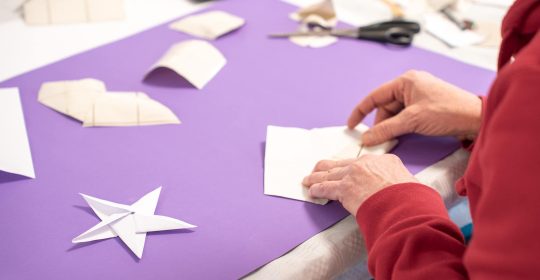 In der Kinderbetreuung vom Familotel Sonnenpark wird mit weißem Geschenkpapier ein Origami-Stern gefaltet