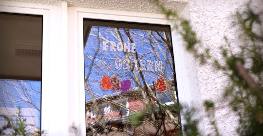 Fenster bemalt mit bunten Ostereiern und "Frohe Ostern"