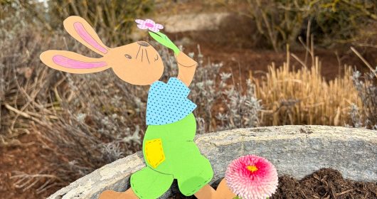 Osterhase aus Tonkarton gebastelt in einem Blumenkasten mit roten Blüten