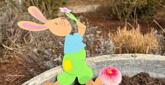 Osterhase aus Tonkarton gebastelt in einem Blumenkasten mit roten Blüten