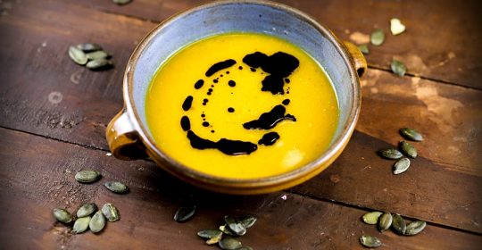 Schüssel auf Holztisch mit Kürbissuppe und Kürbiskernöl darauf