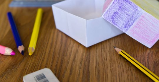 Buntstifte und Radiergummi vor einer Papierkiste auf Holztisch