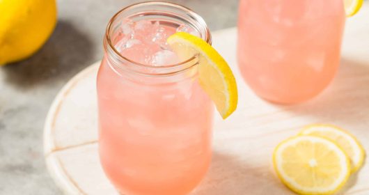 Himbeer-Limonade aus Ginger Bug mit einer Zitronenscheibe im Glas auf einem Holzbrett