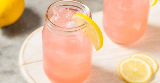 Himbeer-Limonade aus Ginger Bug mit einer Zitronenscheibe im Glas auf einem Holzbrett