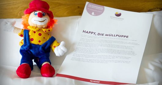 Plüschfigur eines Clowns liegt neben einer Gute Nacht Geschichte auf einem Kopfkissen