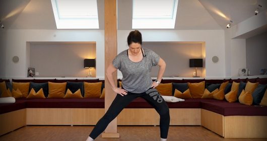 Frau auf blauer Matte macht ein Workout vor einem großen Sofa