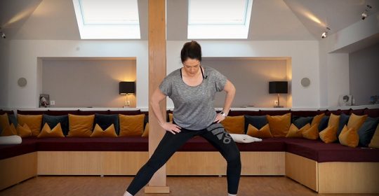 Frau auf blauer Matte macht ein Workout vor einem großen Sofa