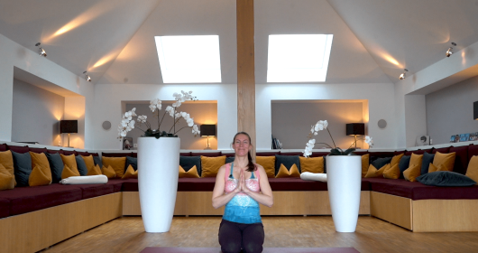 Frau in Yoga-Pose auf einer rosa Matte vor einem großen Sofa