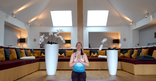 Frau in Yoga-Pose auf einer rosa Matte vor einem großen Sofa