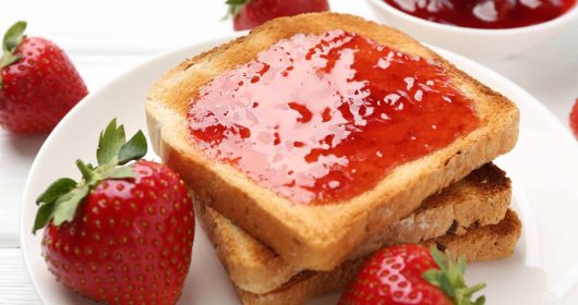 Toastbrot mit zuckerfreier Erdbeermarmelade bestrichen auf einem weißen Teller mit Erdbeeren dekoriert