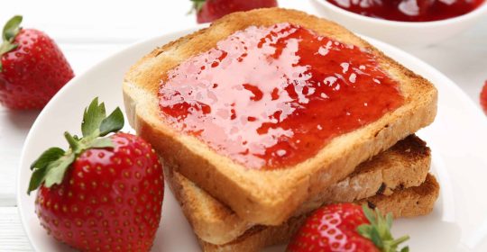 Toastbrot mit zuckerfreier Erdbeermarmelade bestrichen auf einem weißen Teller mit Erdbeeren dekoriert